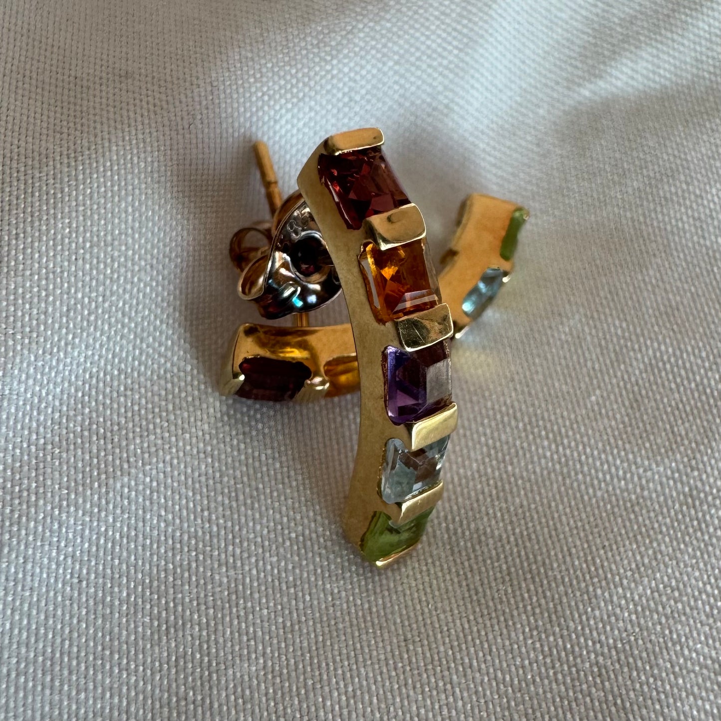 18K gold hoop earrings set with a vibrant line of multi-colored gemstones — including Garnet, Citrine, Amethyst, Peridot, and Blue Topaz.