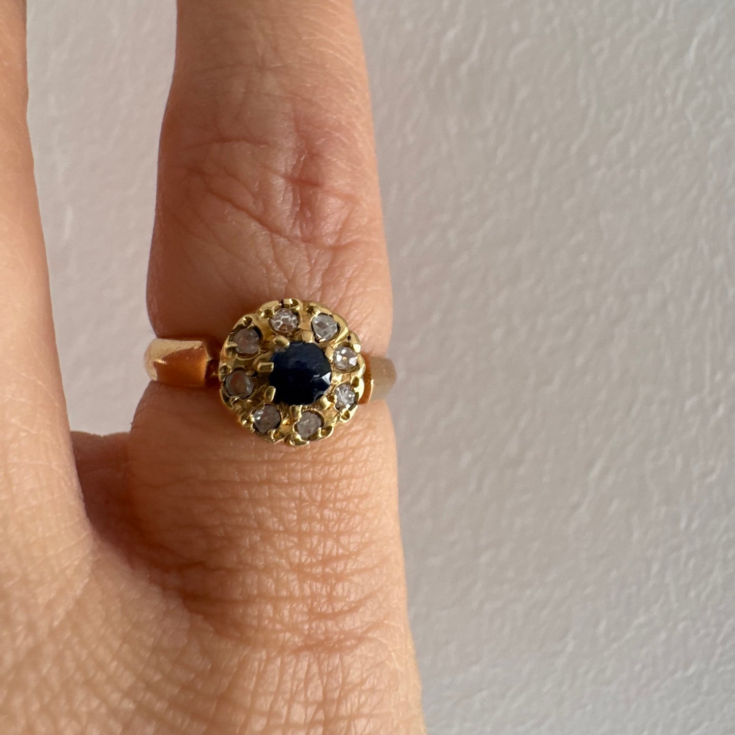 טבעת זהב 14 קראט משובצת ספיר מרכזי מוקף הילה של יהלומים בחיתוך עגול.