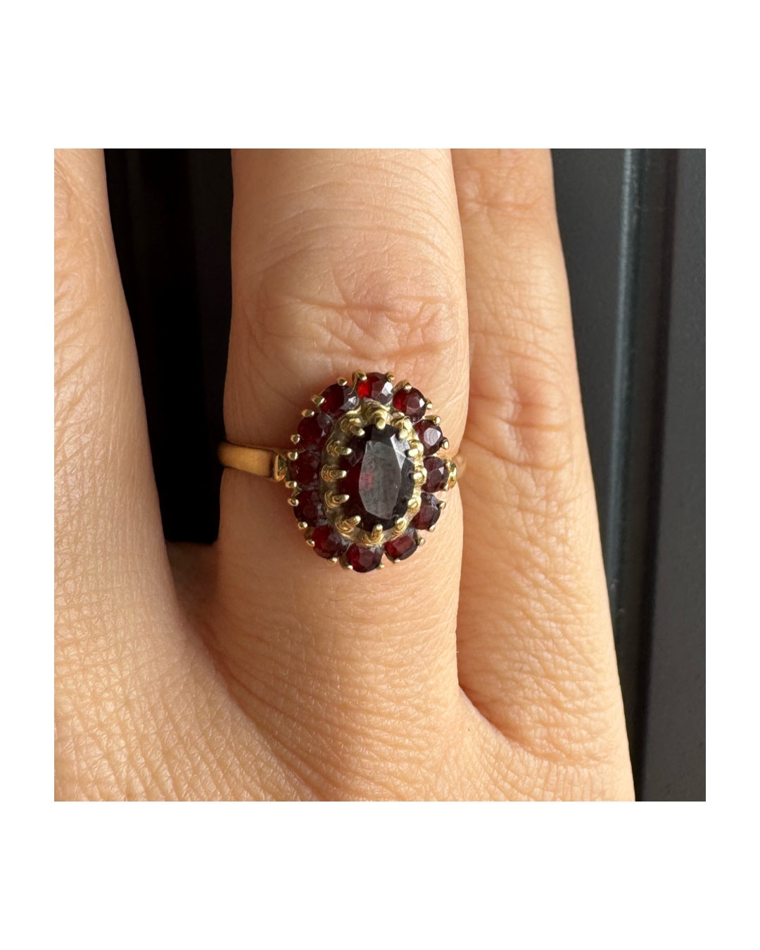 טבעת זהב צהוב 18 קראט משובצת אבן גרנט אובלית במרכז, מוקפת באבני גרנט קטנות בסידור אליפטי קלאסי.