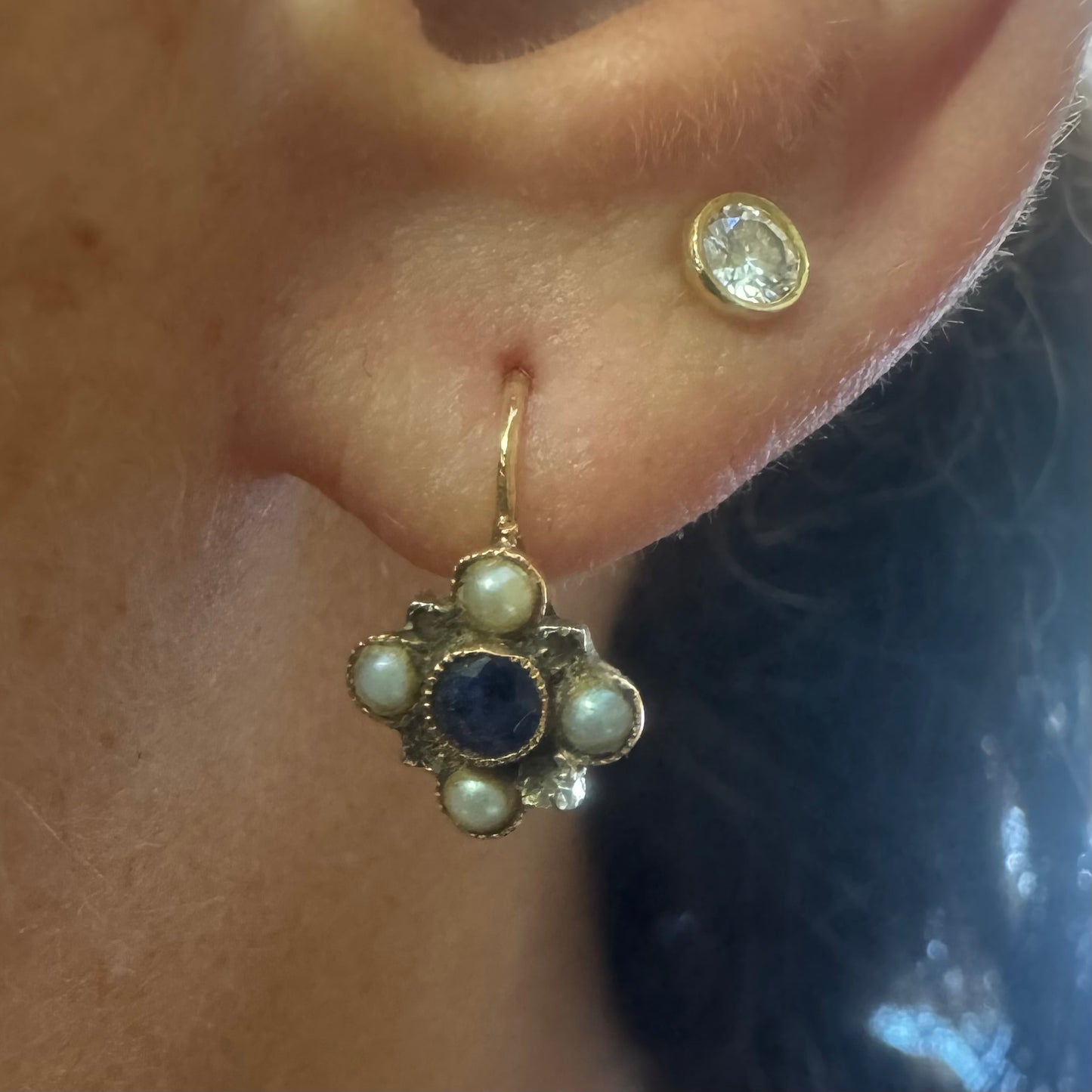 14K gold earrings featuring a round deep blue Sapphire in the center, surrounded by Pearls arranged in a floral design.