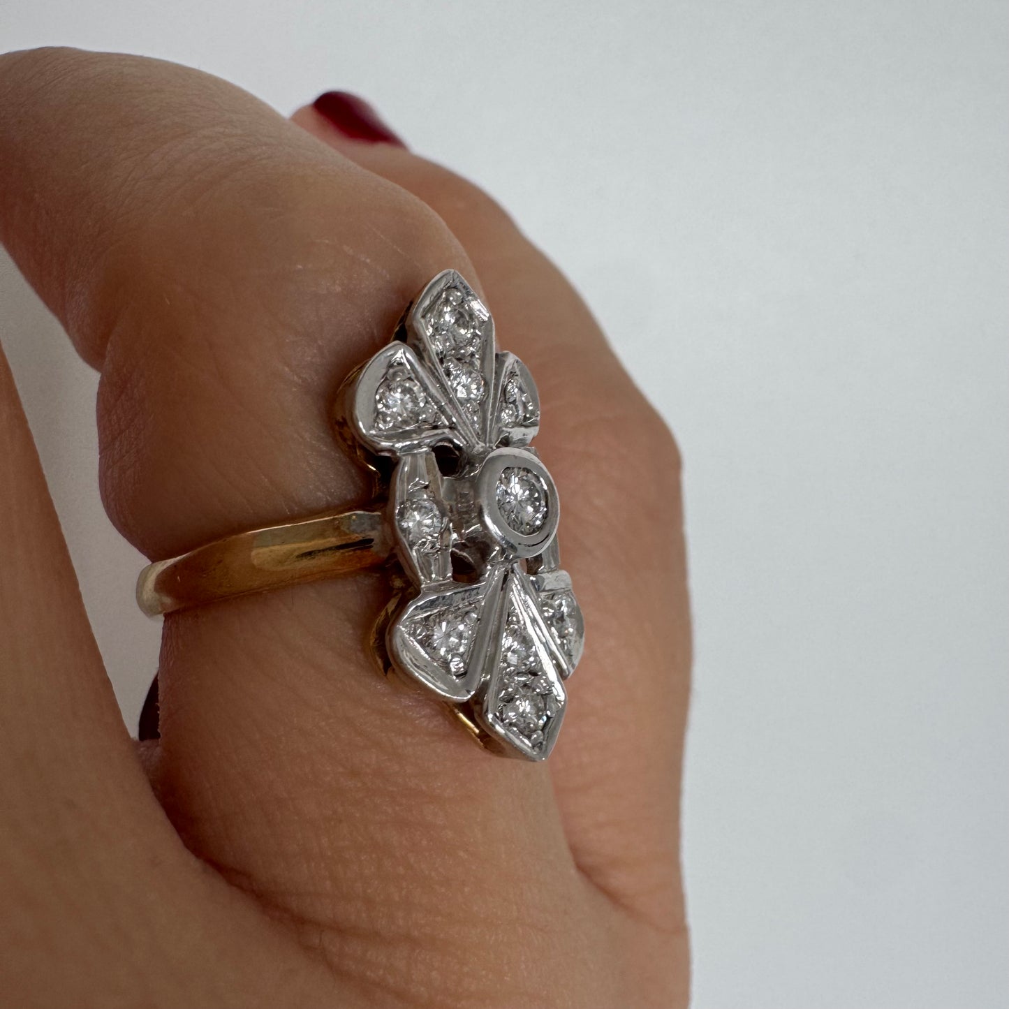 טבעת זהב לבן 14 קראט, בעיצוב אלגנטי ועדין, משובצת יהלום מרכזי עגול וסביבו יהלומים נוצצים נוספים.