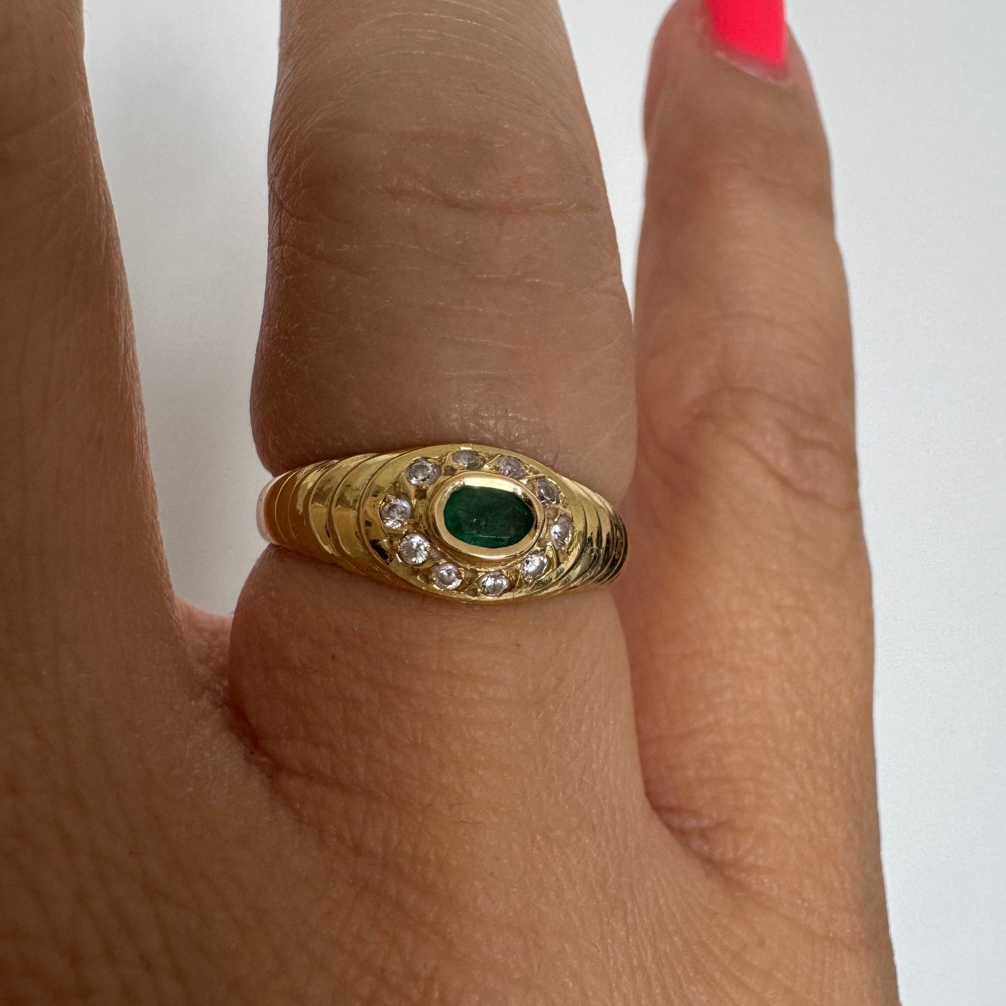 18K gold ring set with an oval Emerald at the center surrounded by Diamonds