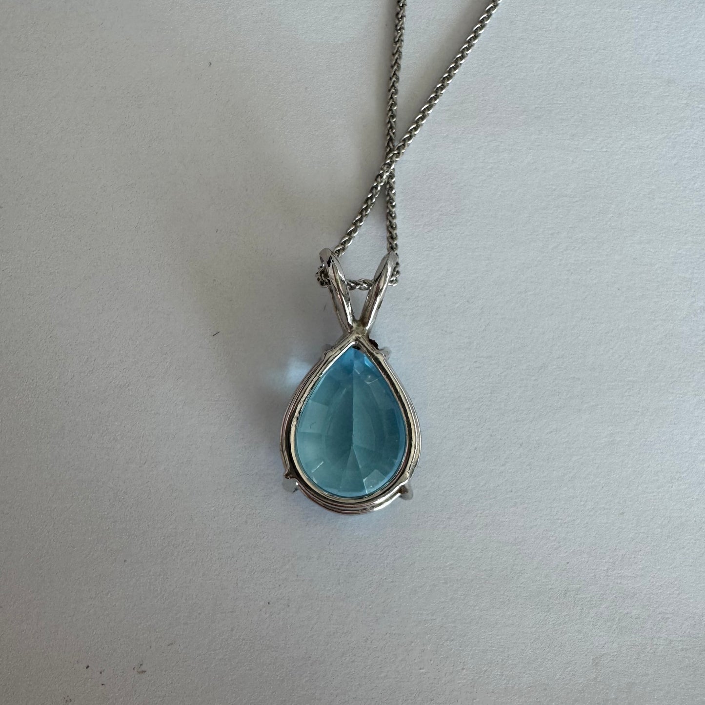 תליון זהב לבן 14 קראט המשובץ אבן טופז כחולה בחיתוך טיפה.