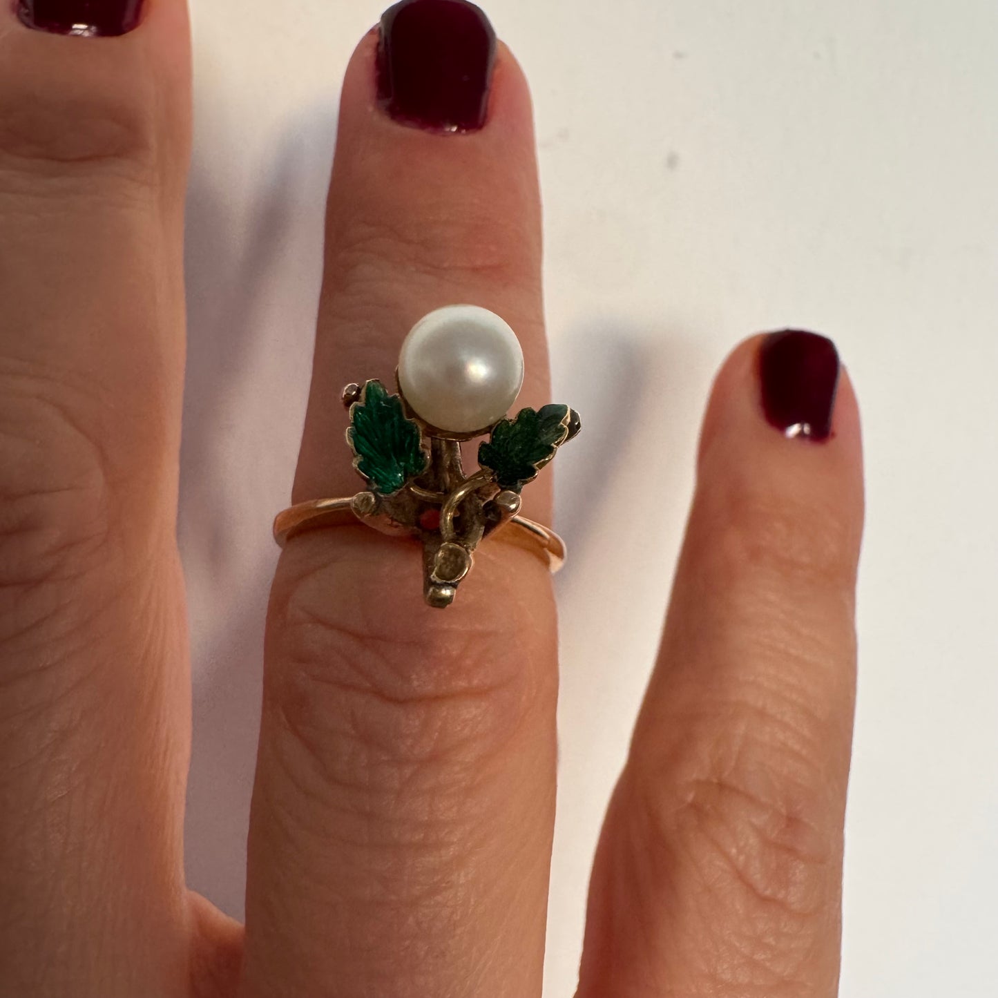 טבעת זהב 14 קראט משובצת פנינה מרכזית ומעוטרת אמייל ירוק בעבודת יד בצורת עלים.