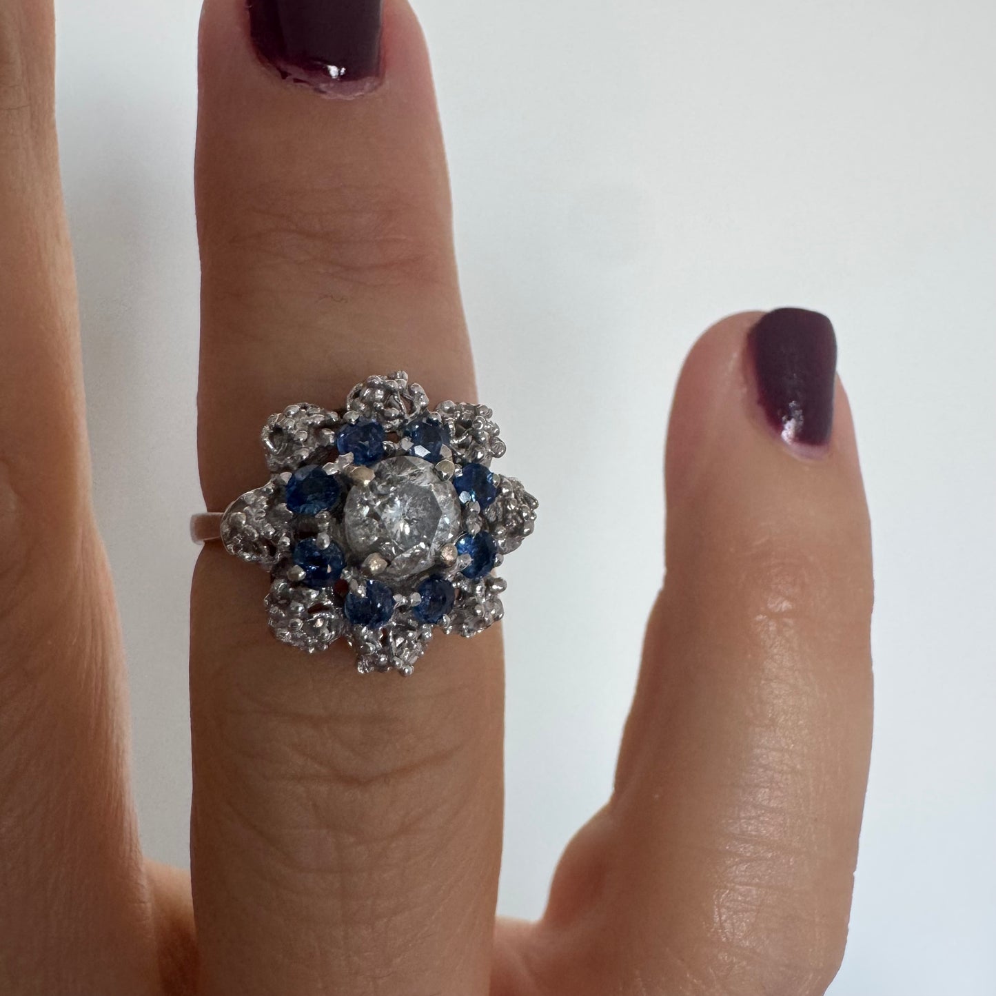 18K gold ring featuring a large round Diamond at the center, surrounded by a floral halo of purple -blue Tanzanite and & Diamonds.