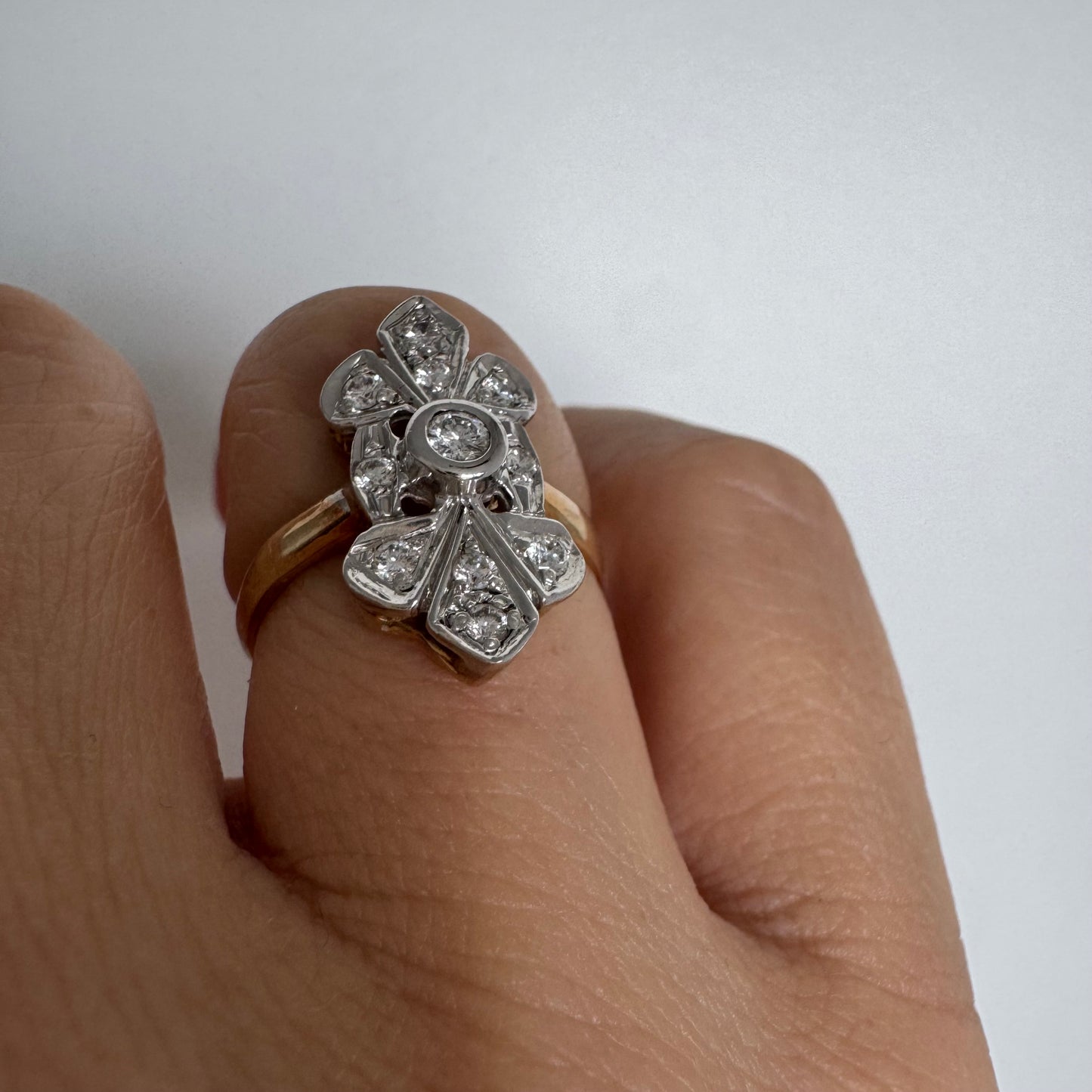 טבעת זהב לבן 14 קראט, בעיצוב אלגנטי ועדין, משובצת יהלום מרכזי עגול וסביבו יהלומים נוצצים נוספים.