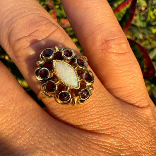 14K gold ring set with a luminous marquise-cut Opal at the center, surrounded by deep red Garnet cabochons