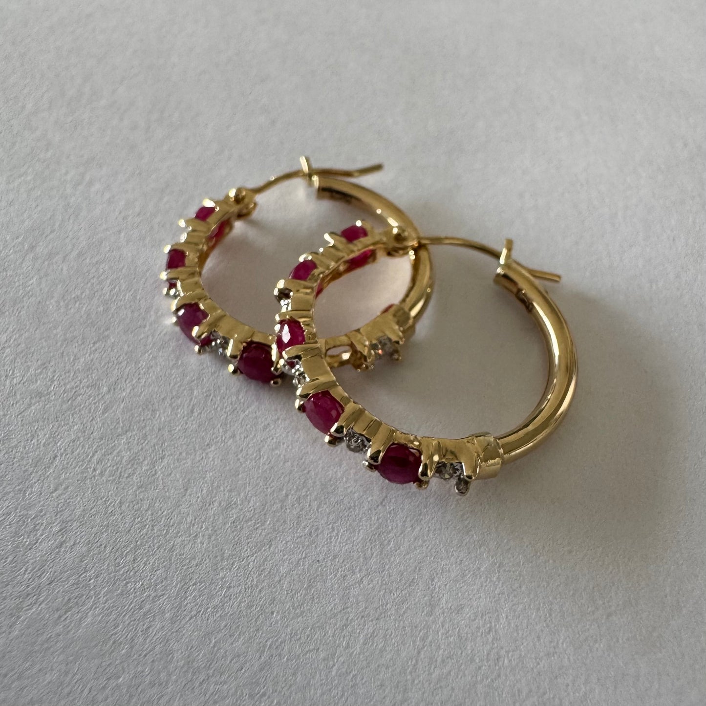 עגילי חישוק זהב צהוב 14 קראט משובצים אבני רובי בגוון אדום עמוק, בשילוב יהלומים המעניקים ברק עדין בין האבנים.