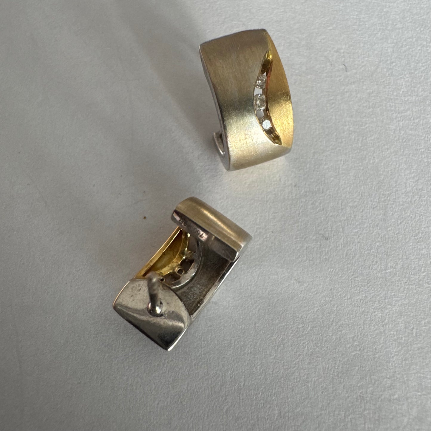 עגילי זהב 18 קראט משובצים יהלומים בעיצוב מודרני ונקי עם שילוב של שני גוונים וגימור מאט יוקרתי.