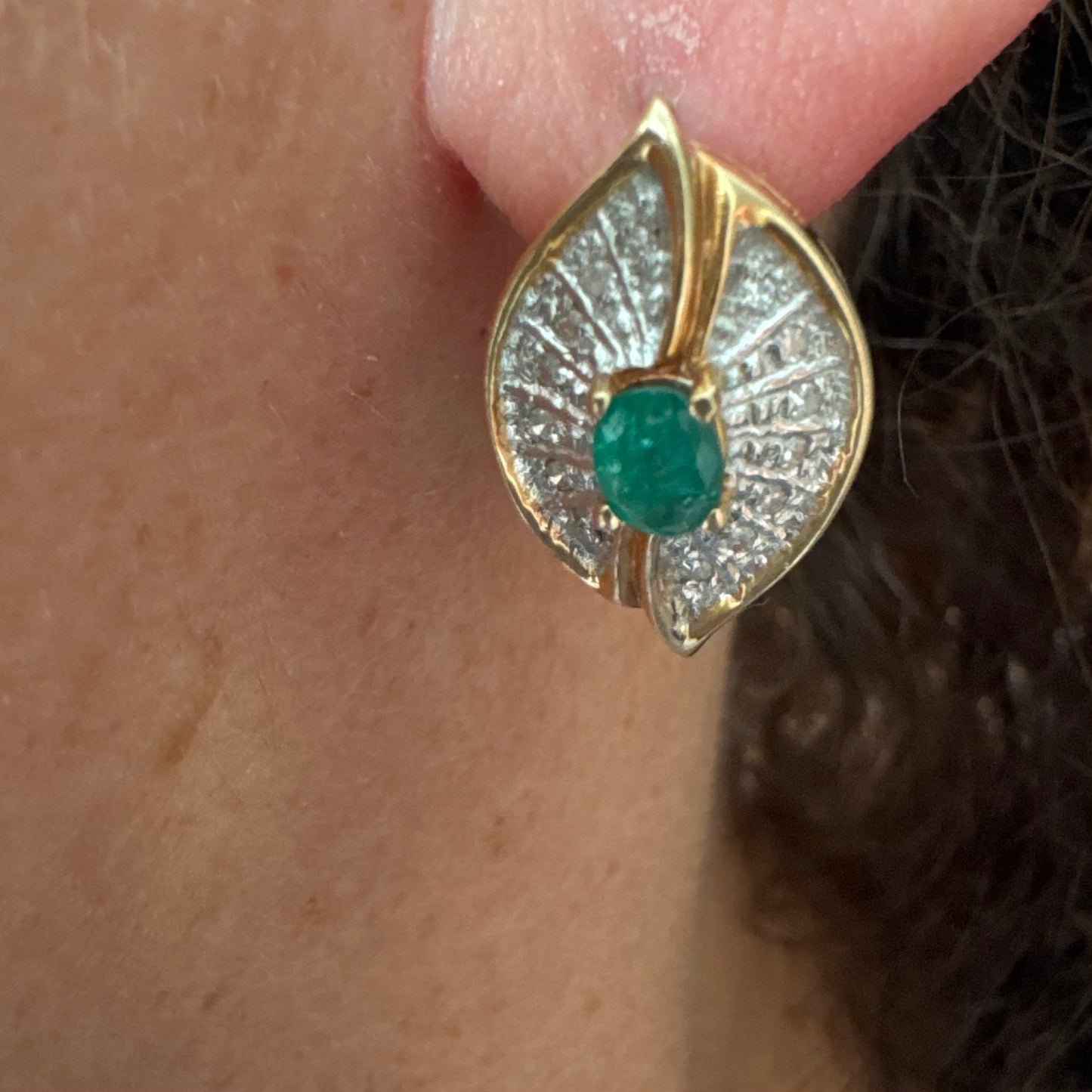 עגילים צמודים לאוזן, זהב צהוב 14 קראט, משובצים אמרלד במרכז, וסביבן פיתוחים משובצים יהלומים, שמעניקים מראה של ניצוץ רך ואלגנטי