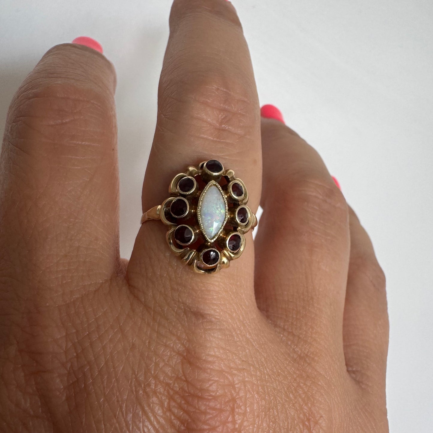 14K gold ring set with a luminous marquise-cut Opal at the center, surrounded by deep red Garnet cabochons