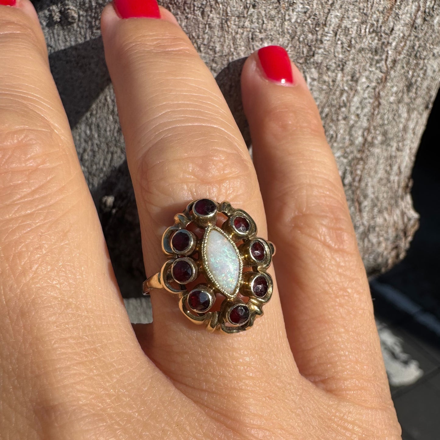 14K gold ring set with a luminous marquise-cut Opal at the center, surrounded by deep red Garnet cabochons