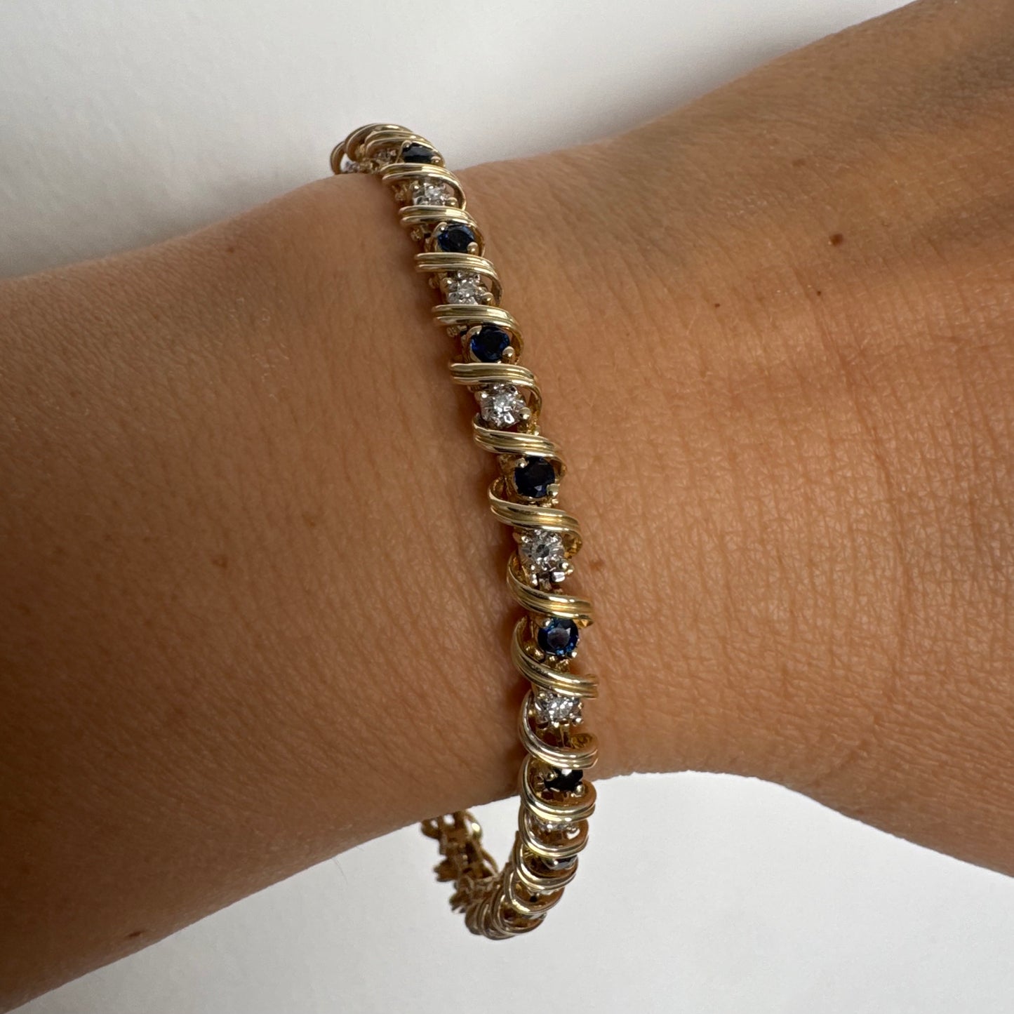 צמיד זהב צהוב 14 קראט משובץ אבני ספיר כחולות ויהלומים, המשובצים בעיצוב זורם עם קווים מעוגלים העוטפים כל אבן.