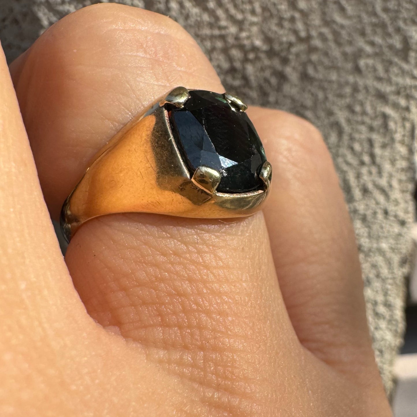 טבעת זהב 9 קראט משובצת ספיר ירוק כהה בחיתוך כרית ובתפסים עבים, בעיצוב נקי ובעל נוכחות. 