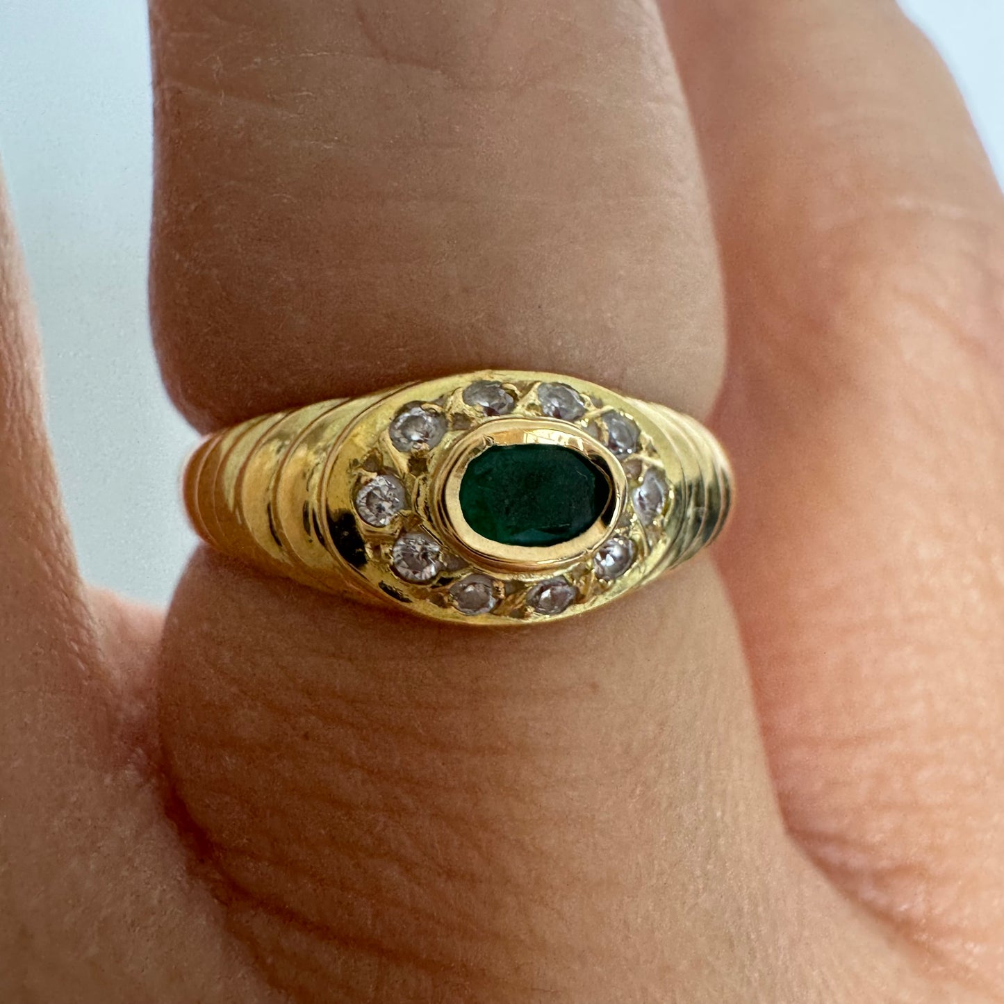 18K gold ring set with an oval Emerald at the center surrounded by Diamonds