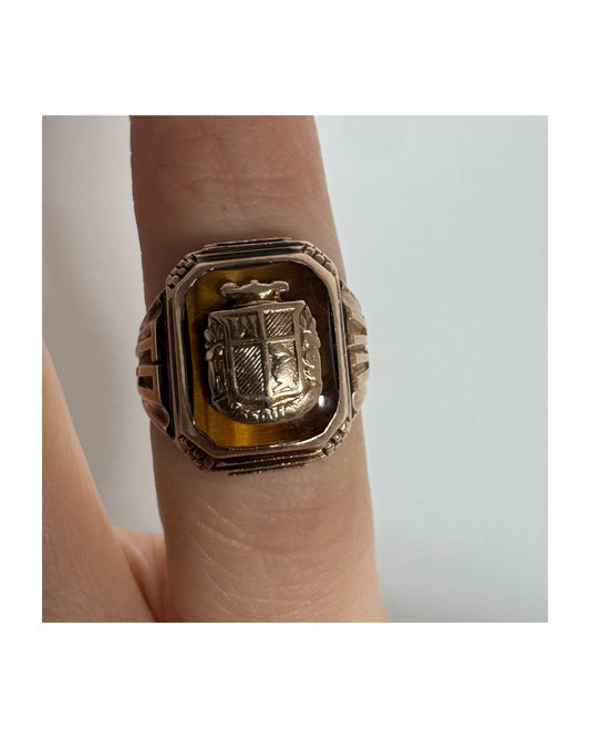 טבעת חותם זהב צהוב 10 קראט עם אבן בגוון חום-דבש ועיטור סמל מובלט במרכז.