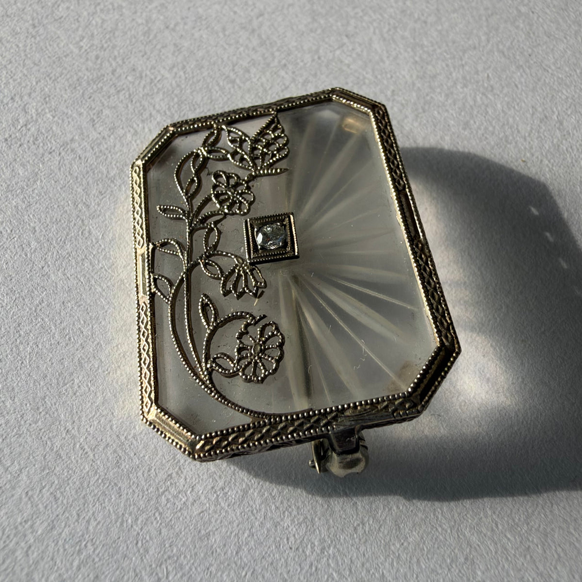 An antique Art-Deco brooch featuring a geometric design, delicate floral details & a sparkling Diamond