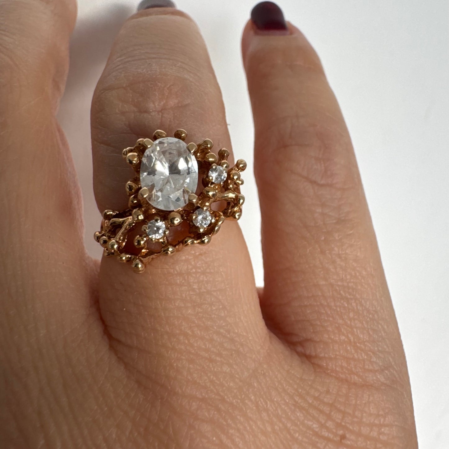 14K gold ring set with a central oval clear stone, accented by additional clear stones in an open, organic design.