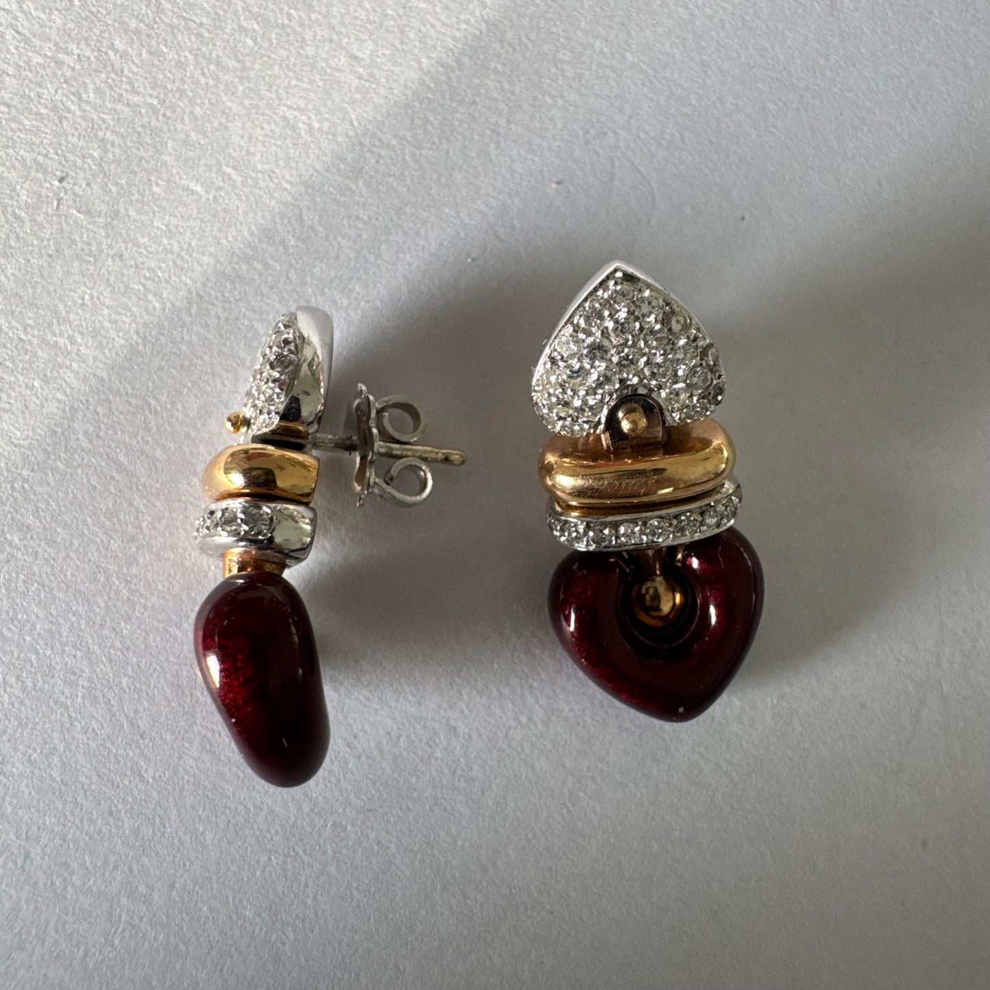 עגילי זהב 18 קראט בשילוב זהב צהוב ולבן, משובצים יהלומים בחלק העליון ובחישוק מרכזי, ובתחתית תליון לב אדום בגימור מבריק.