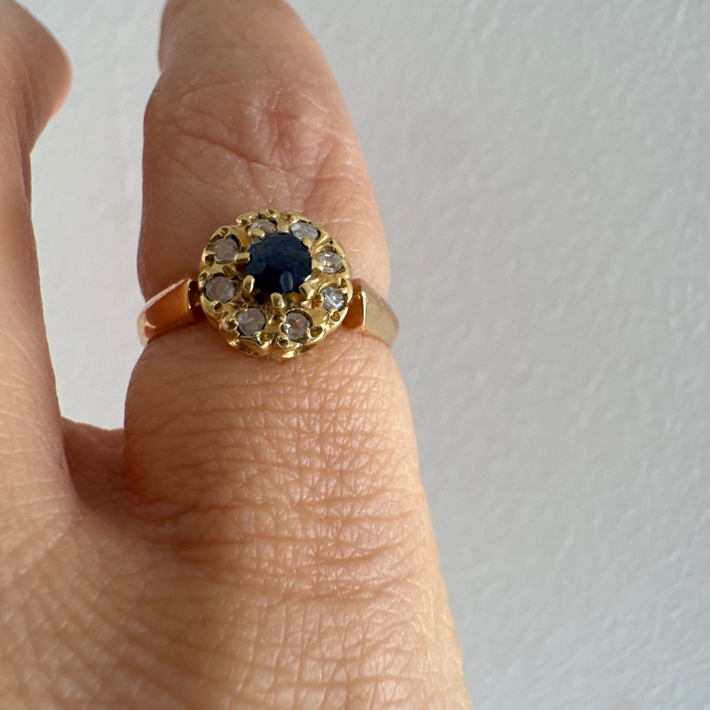 טבעת זהב 14 קראט משובצת ספיר מרכזי מוקף הילה של יהלומים בחיתוך עגול.