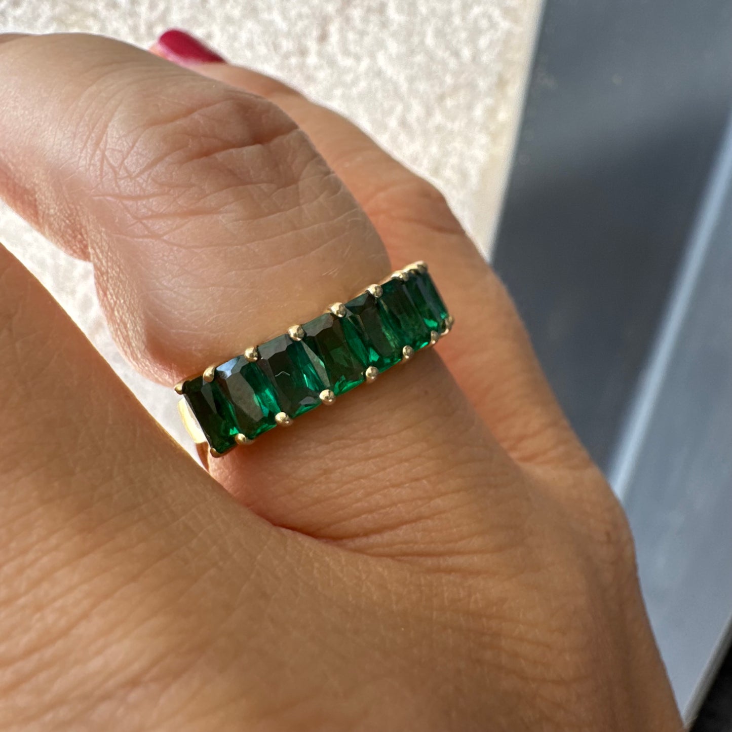 טבעת זהב צהוב 14 קראט משובצת אבנים ירוקות בחיתוך אמרלד, בעיצוב חצי איטרניטי.