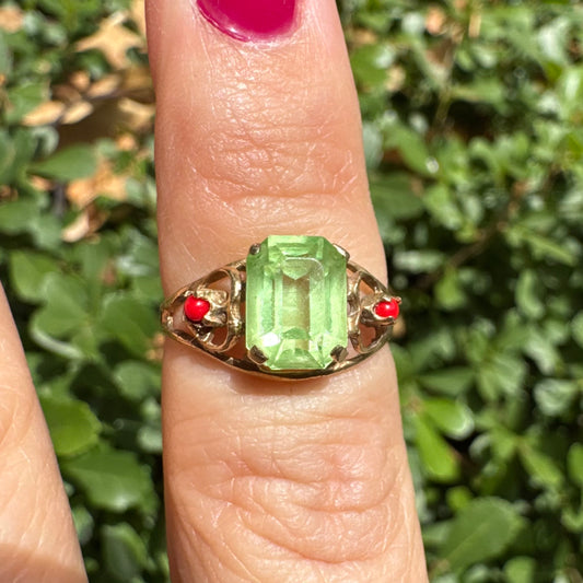14K gold ring set with a vibrant emerald-cut Peridot at its center, flanked by two delicate red Coral accents