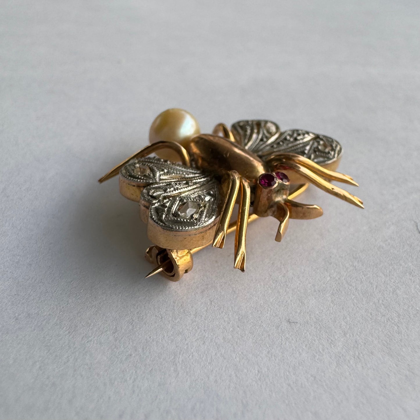 סיכת חרק ייחודית עשויה זהב 14 קראט משובצת יהלומים בעבודת פיליגרן עדינה בכנפיים, אבני רובי אדומות בעיניים ופנינה טבעית בגוון שמפניה.