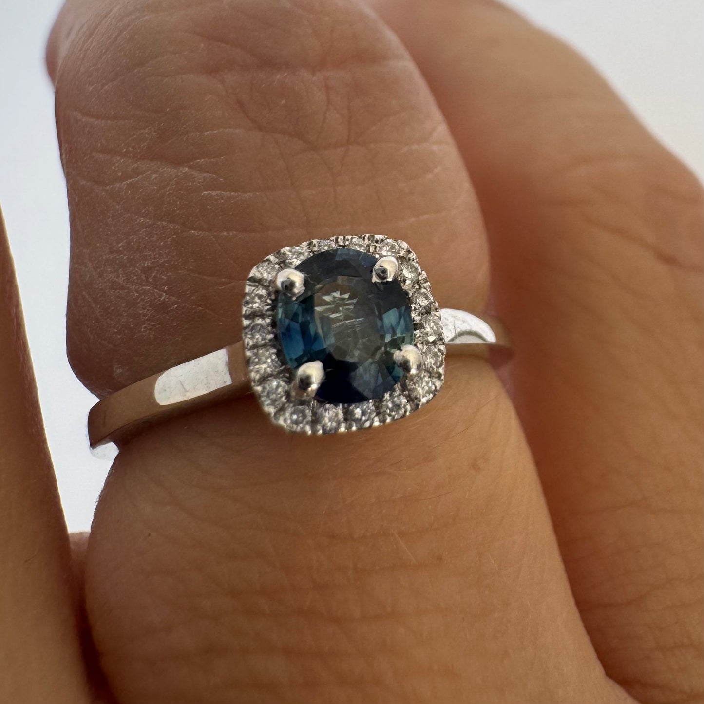 14K gold ring set with an oval blue Sapphire at the center framed by a delicate halo of sparkling Diamonds.