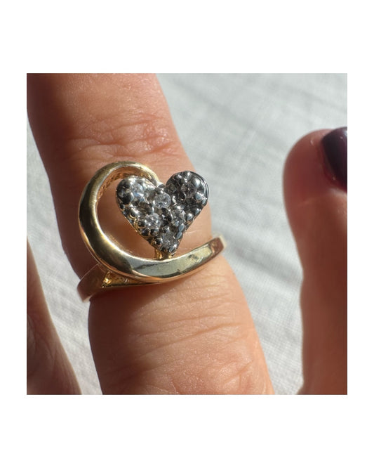 טבעת זהב צהוב 14 קראט ייחודית בעיצוב לב משובץ יהלומים נוצצים, עטופה בקו מוזהב זורם שמעניק תחושת תנועה וחיבוק עדין.