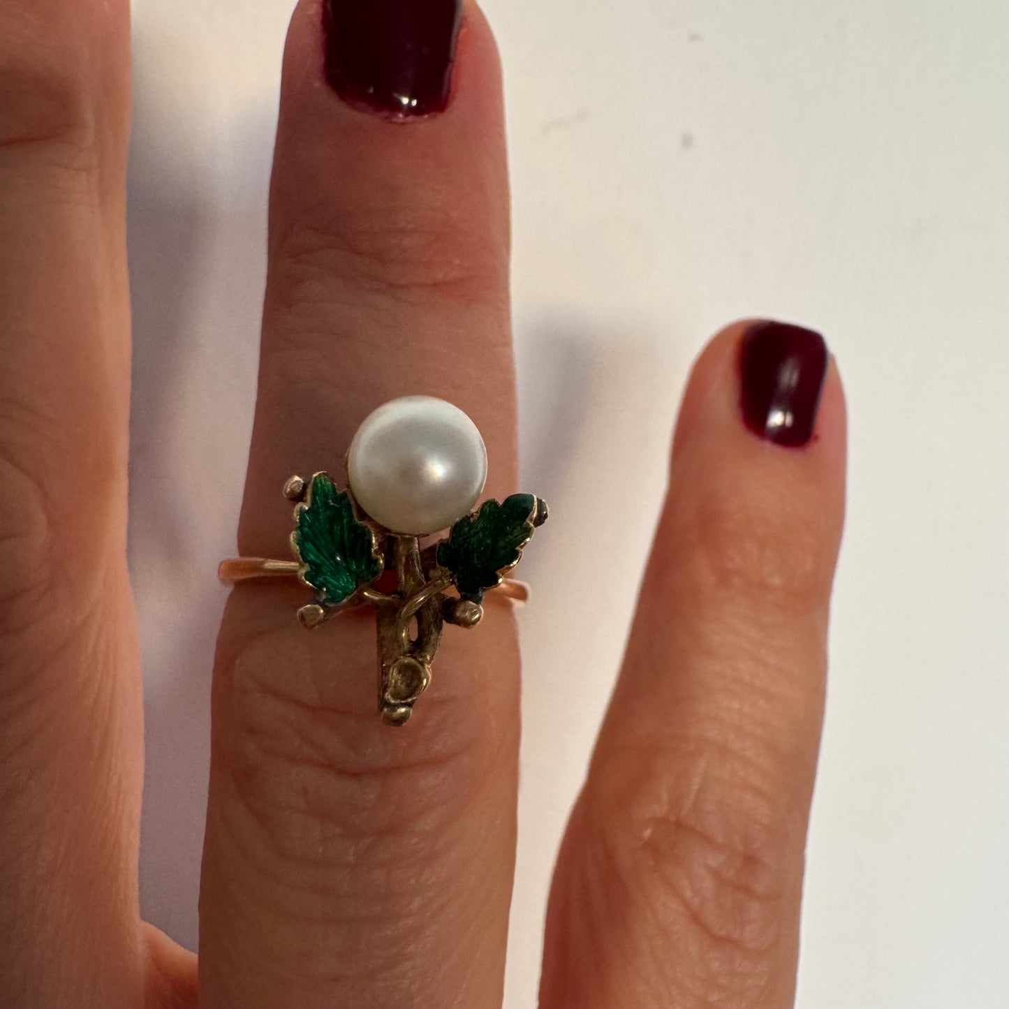 טבעת זהב 14 קראט משובצת פנינה מרכזית ומעוטרת אמייל ירוק בעבודת יד בצורת עלים.