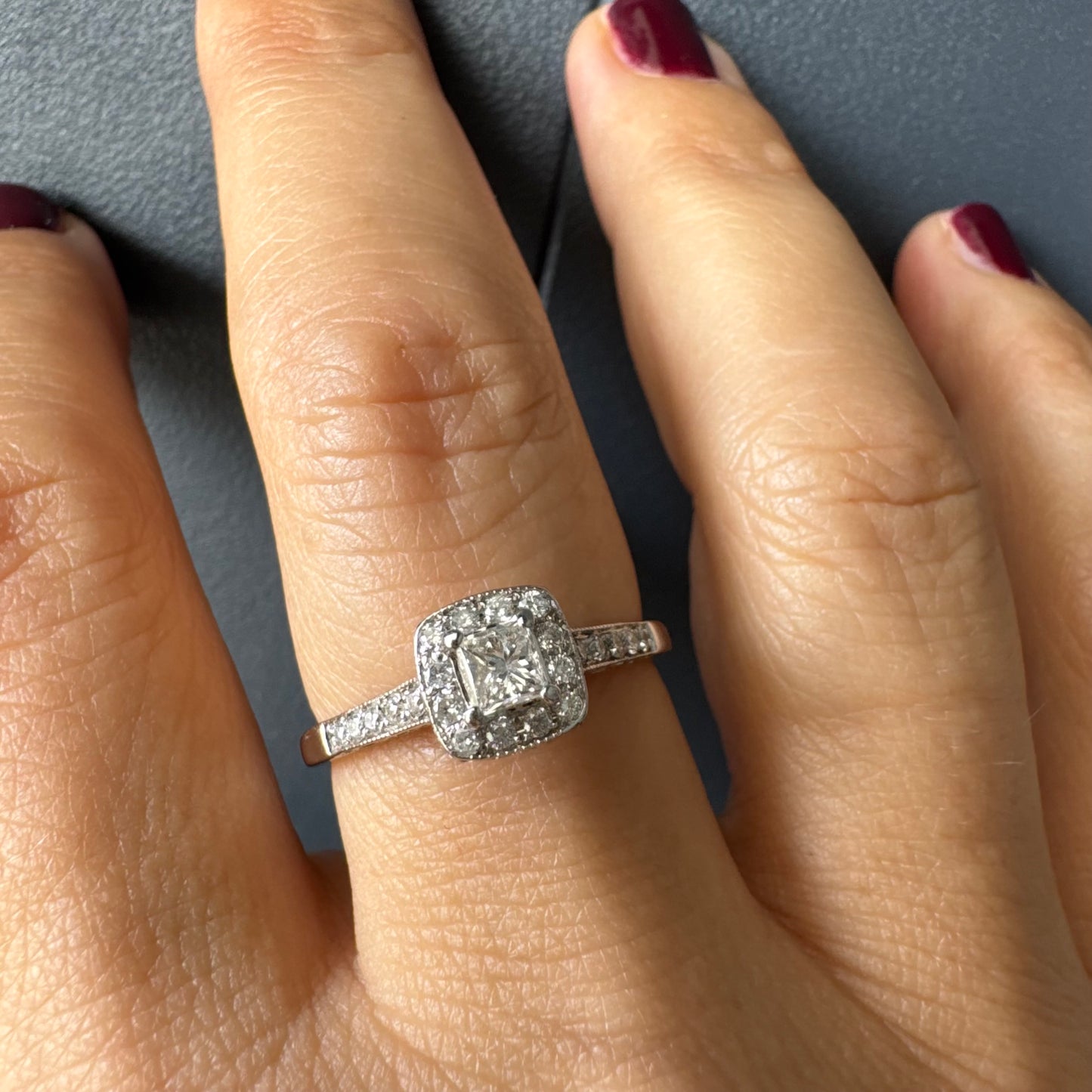 טבעת זהב לבן 14 קראט משובצת יהלום מרכזי בחיתוך פרינסס, מוקף הילת יהלומים קטנים וזרוע משובצת פאווה