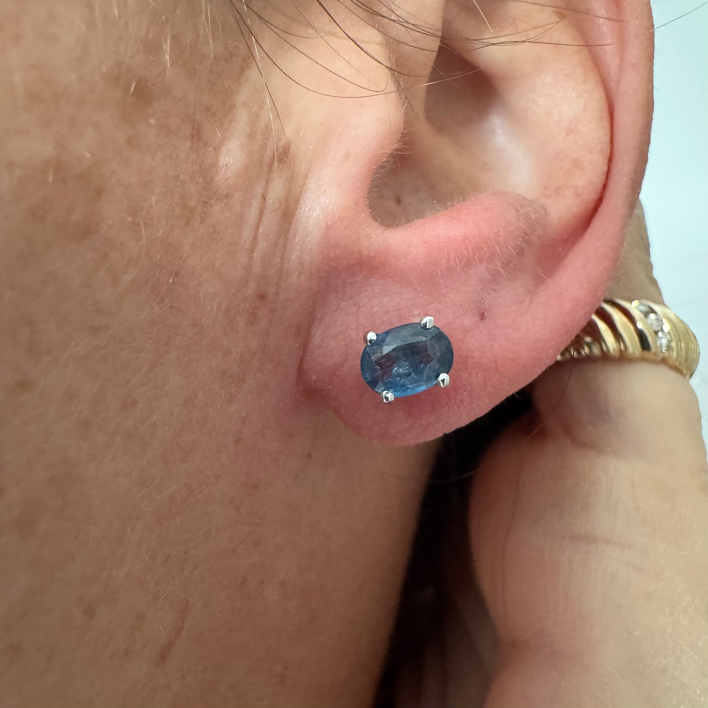 עגילי זהב לבן 14 קראט משובצים אבני טופז כחולות בחיתוך אובלי.