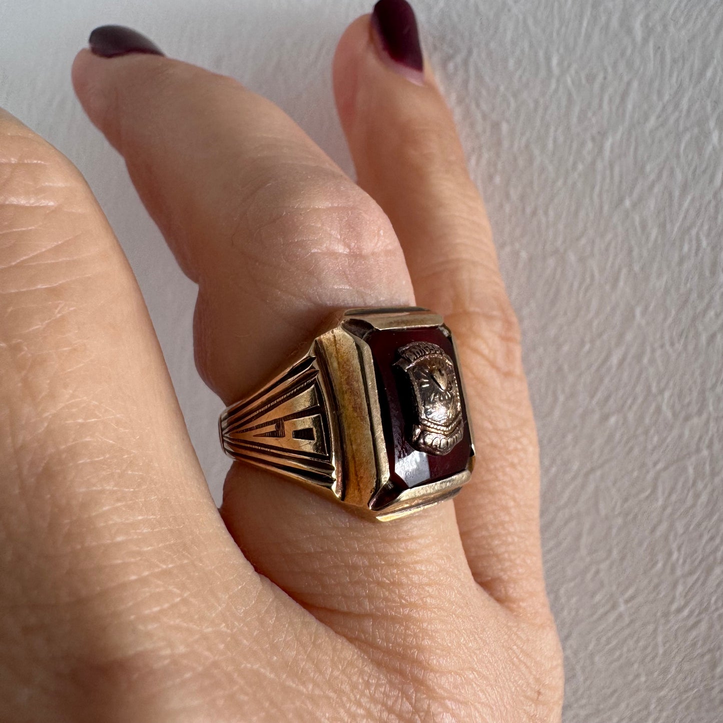 טבעת חותם זהב 10 קראט עם לוח מרכזי בגוון בורדו עמוק ועיטור סמל מובלט.