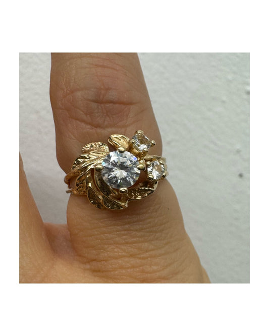טבעת זהב צהוב 14 קראט בעלת עיצוב אורגני עשיר עם עלים מגולפים סביב שלוש אבנים שקופות נוצצות. (לא יהלומים)