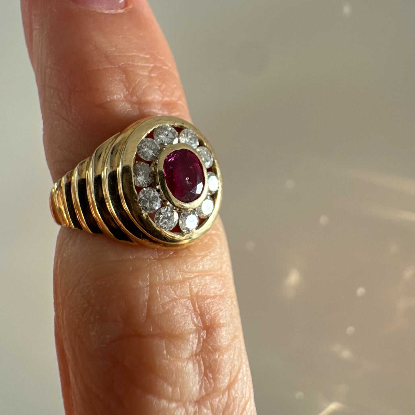 טבעת זהב צהוב 14 קראט בסגנון חותם עגול, משובצת אבן רובי מרכזית וסביבה הילה של יהלומים עגולים.