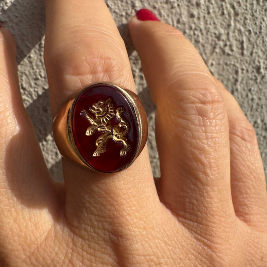 טבעת חותם זהב צהוב 14 קראט משובצת אבן אדומה חלקה ודמות אריה מוזהבת בעיצוב עתיק.