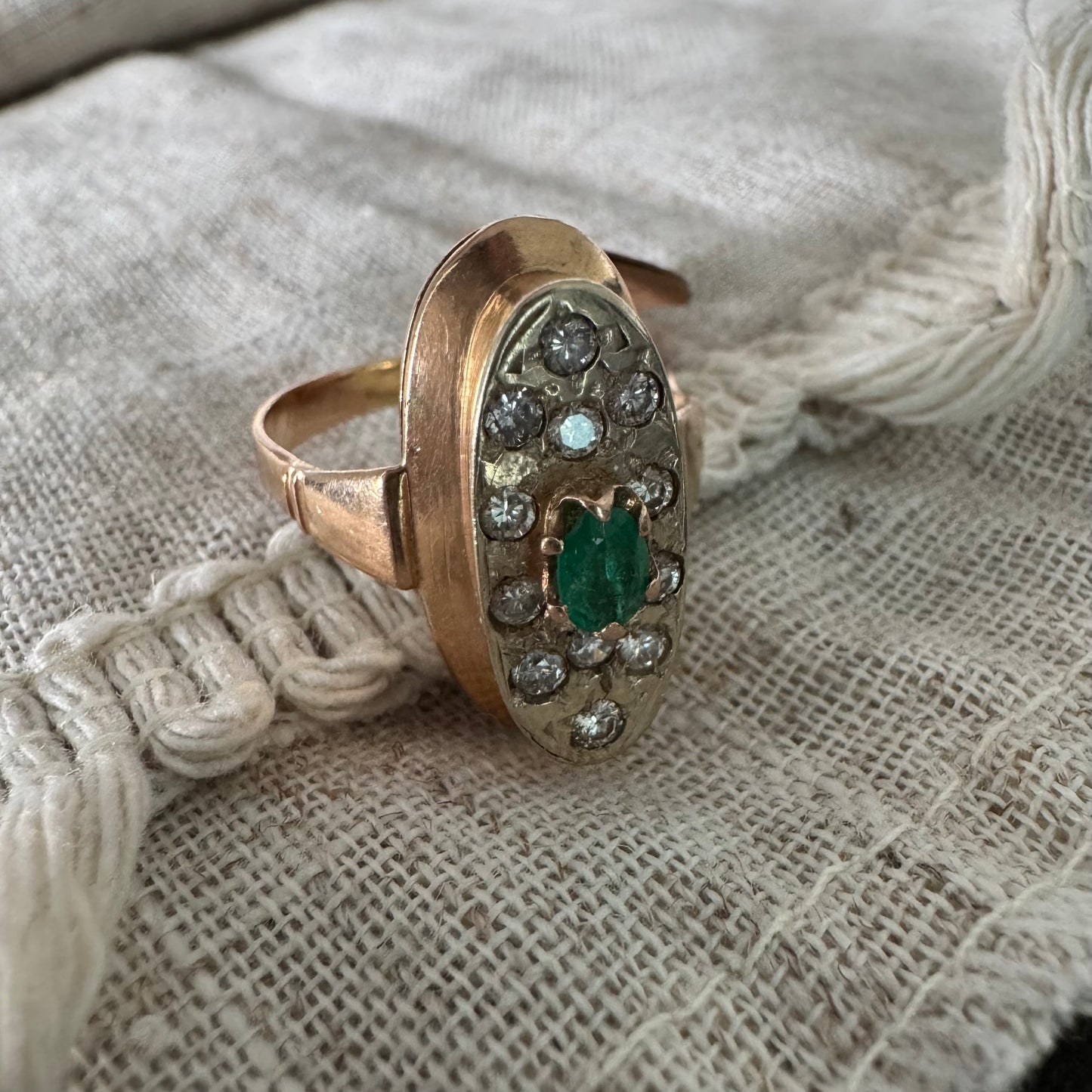 טבעת זהב 14 קראט בעיצוב אלגנטי ומאורך, משובצת אבן אמרלד מרכזית ויהלומים מסביב.