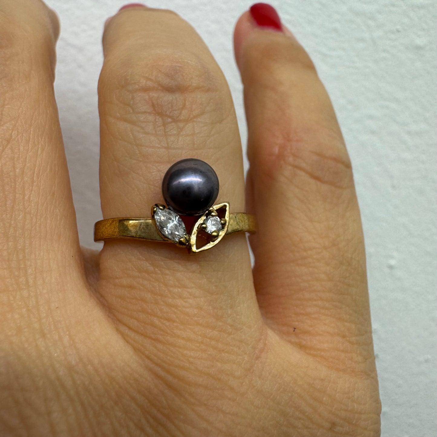 14K gold ring set with a Black Pearl at the center and clear gemstones on the sides.