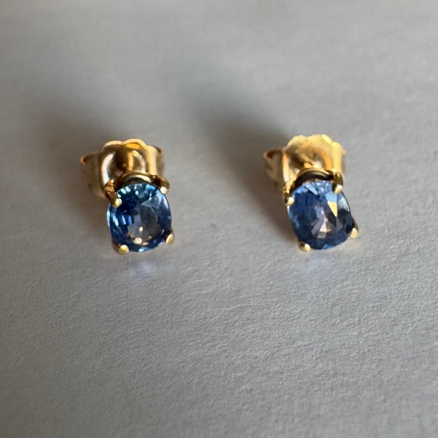 עגילי זהב 14 קראט קטנים צמודים לאוזן משובצים אבני טנזנייט בחיתוך אובלי, בגוון כחול־סגלגל עמוק ומעודן.