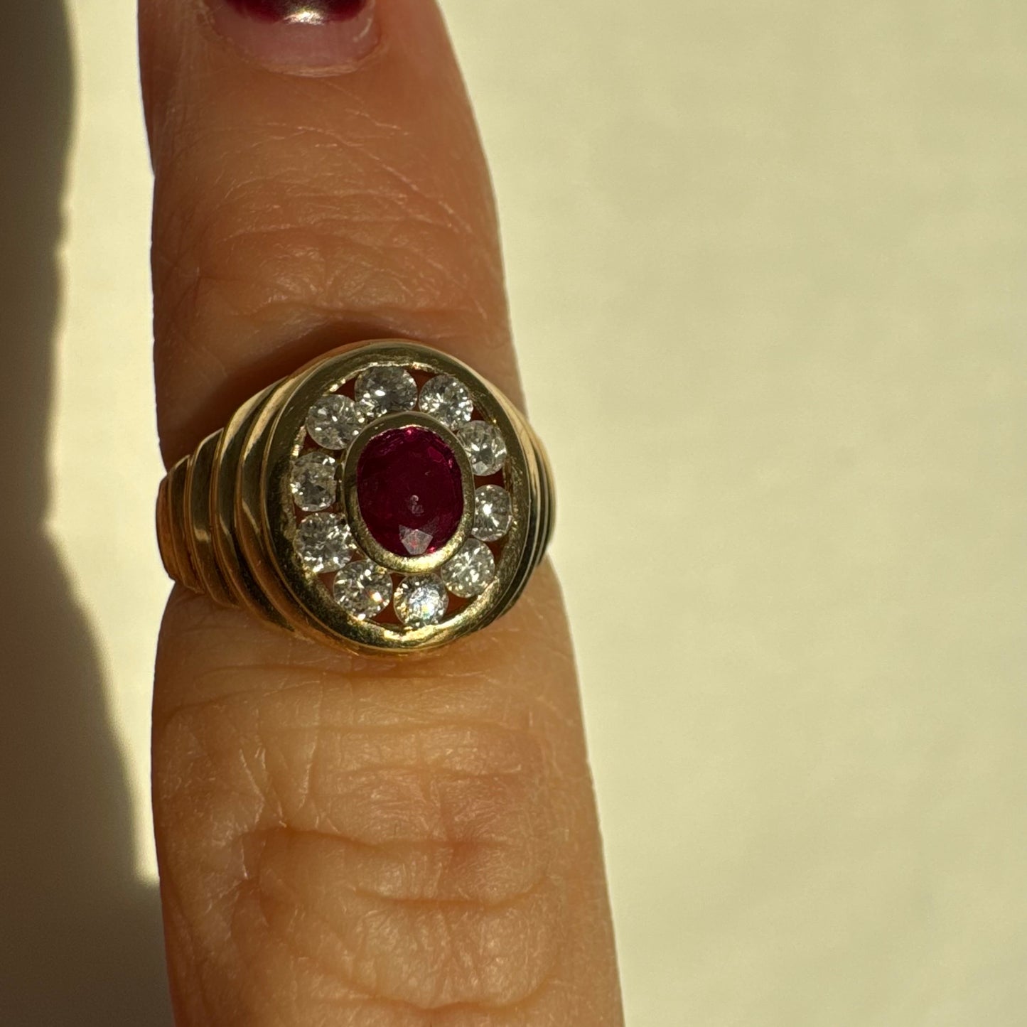 טבעת זהב צהוב 14 קראט בסגנון חותם עגול, משובצת אבן רובי מרכזית וסביבה הילה של יהלומים עגולים.