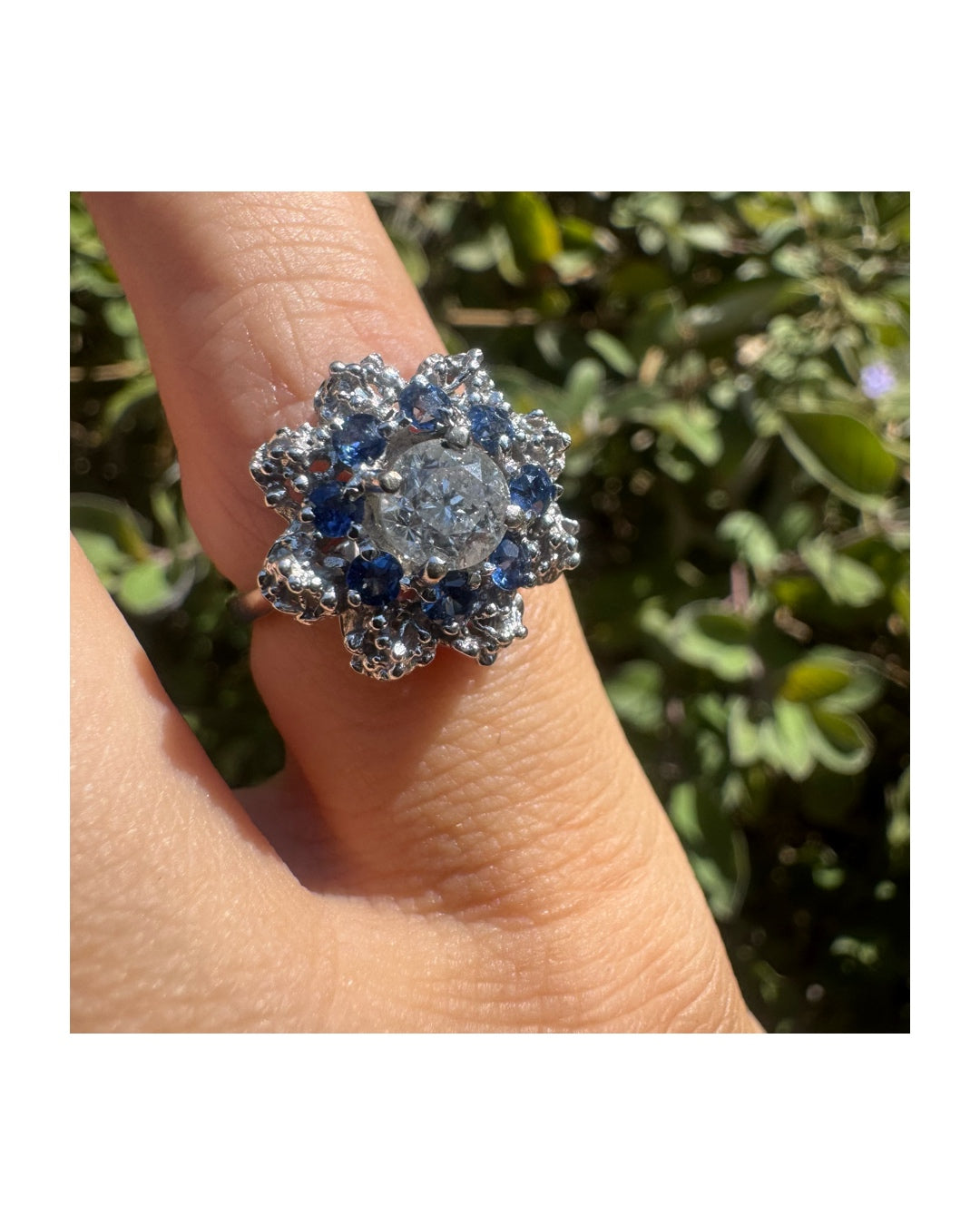 18K gold ring featuring a large round Diamond at the center, surrounded by a floral halo of purple -blue Tanzanite and & Diamonds.