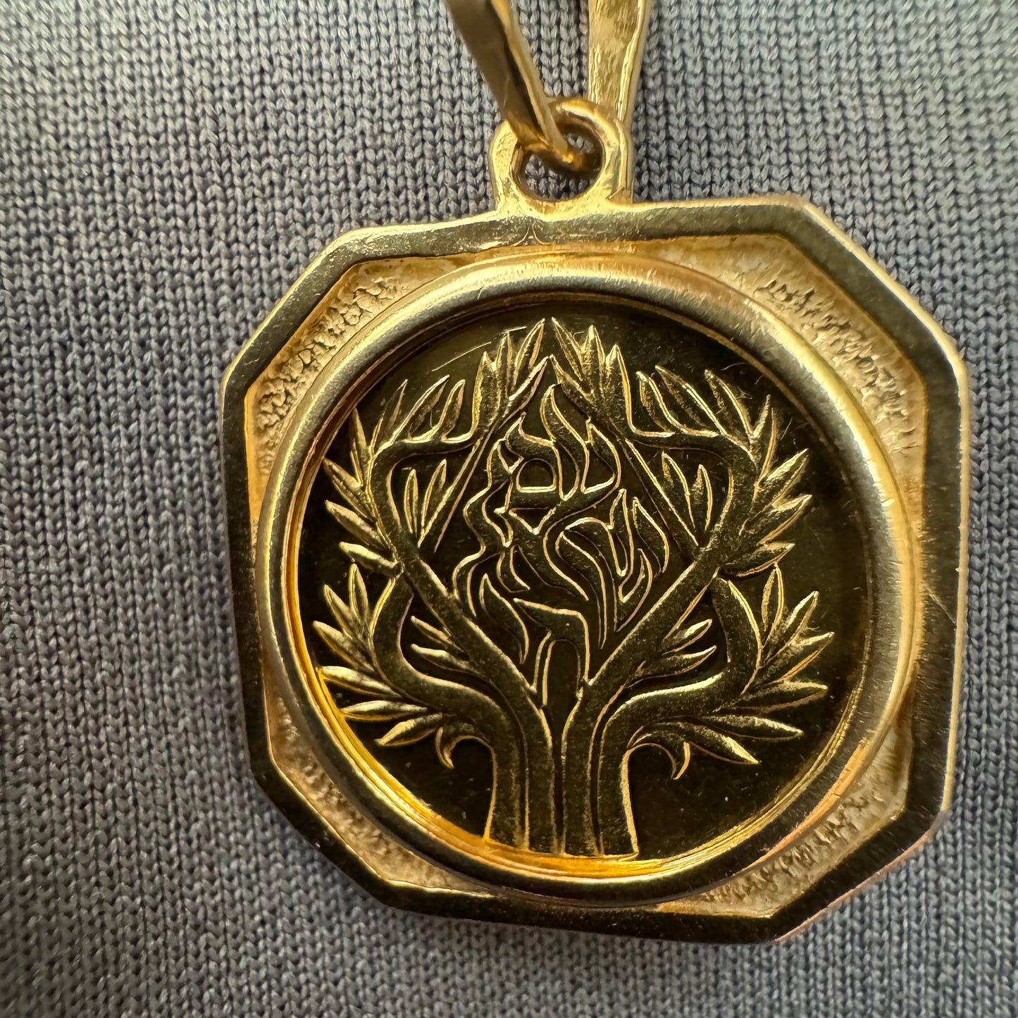 תליון זהב צהוב 14 קראט בעיצוב קלאסי עם נוכחות סמלית חזקה. במרכז התליון חריטה עדינה של עץ חיים, סמל לצמיחה, חיבור ושפע וכיתוב ״שמע ישראל״ ובצד השני אותיות ה-א״ב.