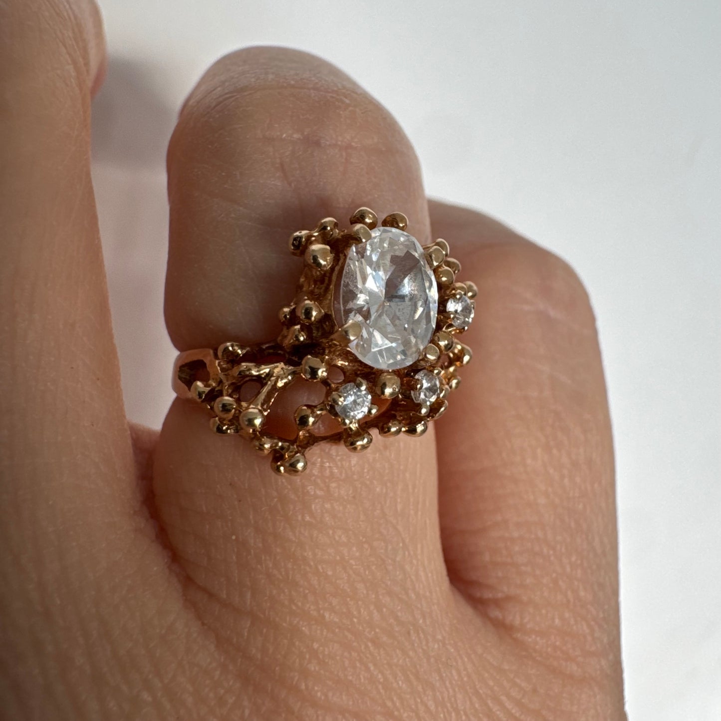 14K gold ring set with a central oval clear stone, accented by additional clear stones in an open, organic design.