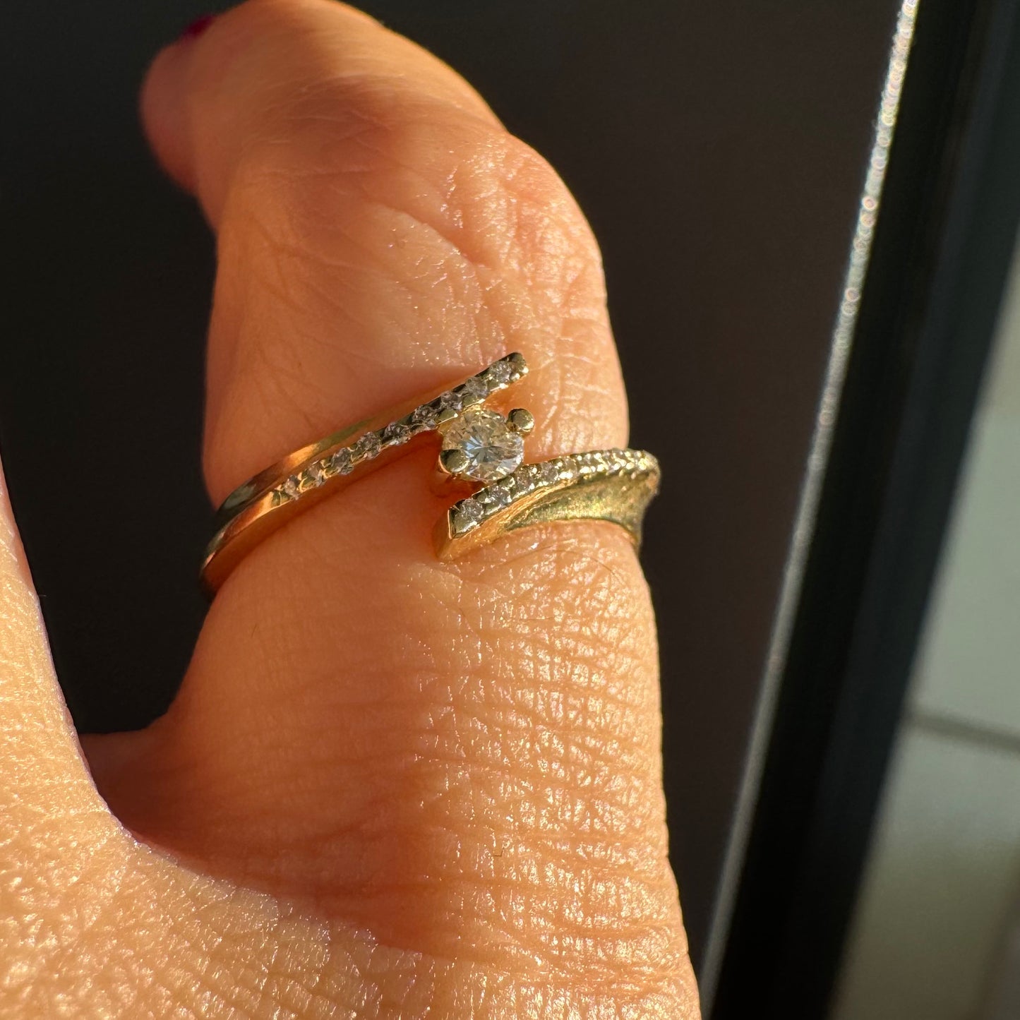 טבעת זהב 14 קראט בעיצוב פתוח ואלגנטי, משובצת יהלום מרכזי ויהלומים עדינים לאורך הזרועות.