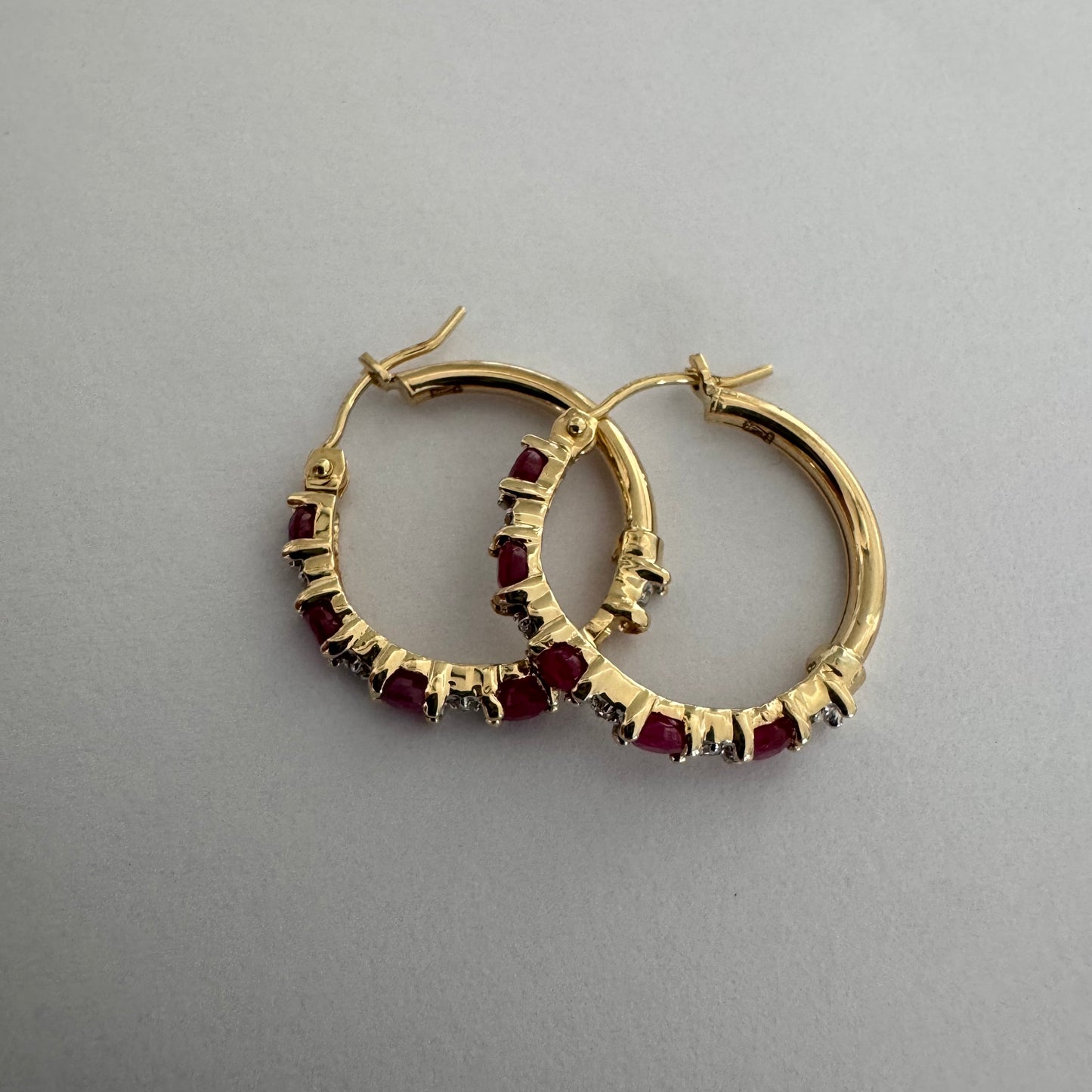 עגילי חישוק זהב צהוב 14 קראט משובצים אבני רובי בגוון אדום עמוק, בשילוב יהלומים המעניקים ברק עדין בין האבנים.