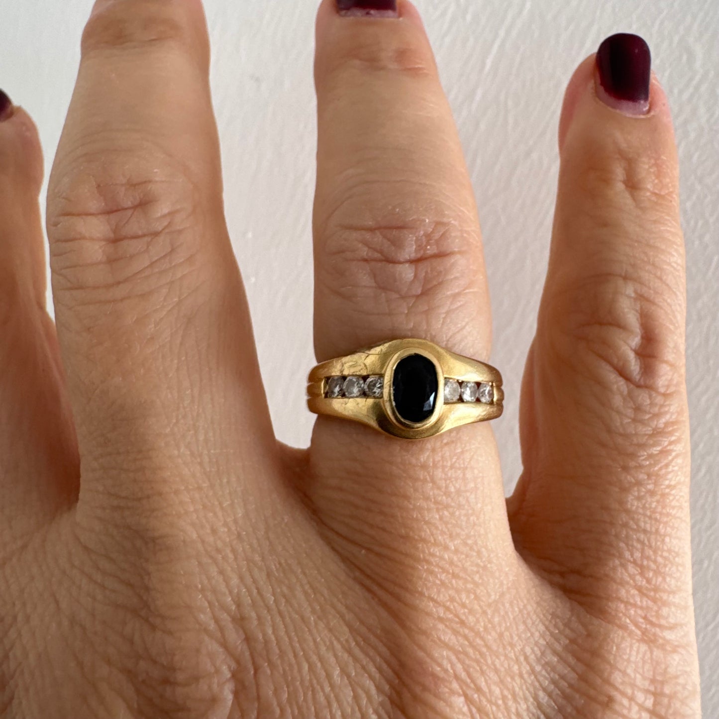 טבעת זהב צהוב 18 קראט משובצת אבן ספיר אובלית בגוון כחול עמוק, במסגרת חלקה ומודגשת, ומשני צדדיה שורת יהלומים משובצים בתעלה.