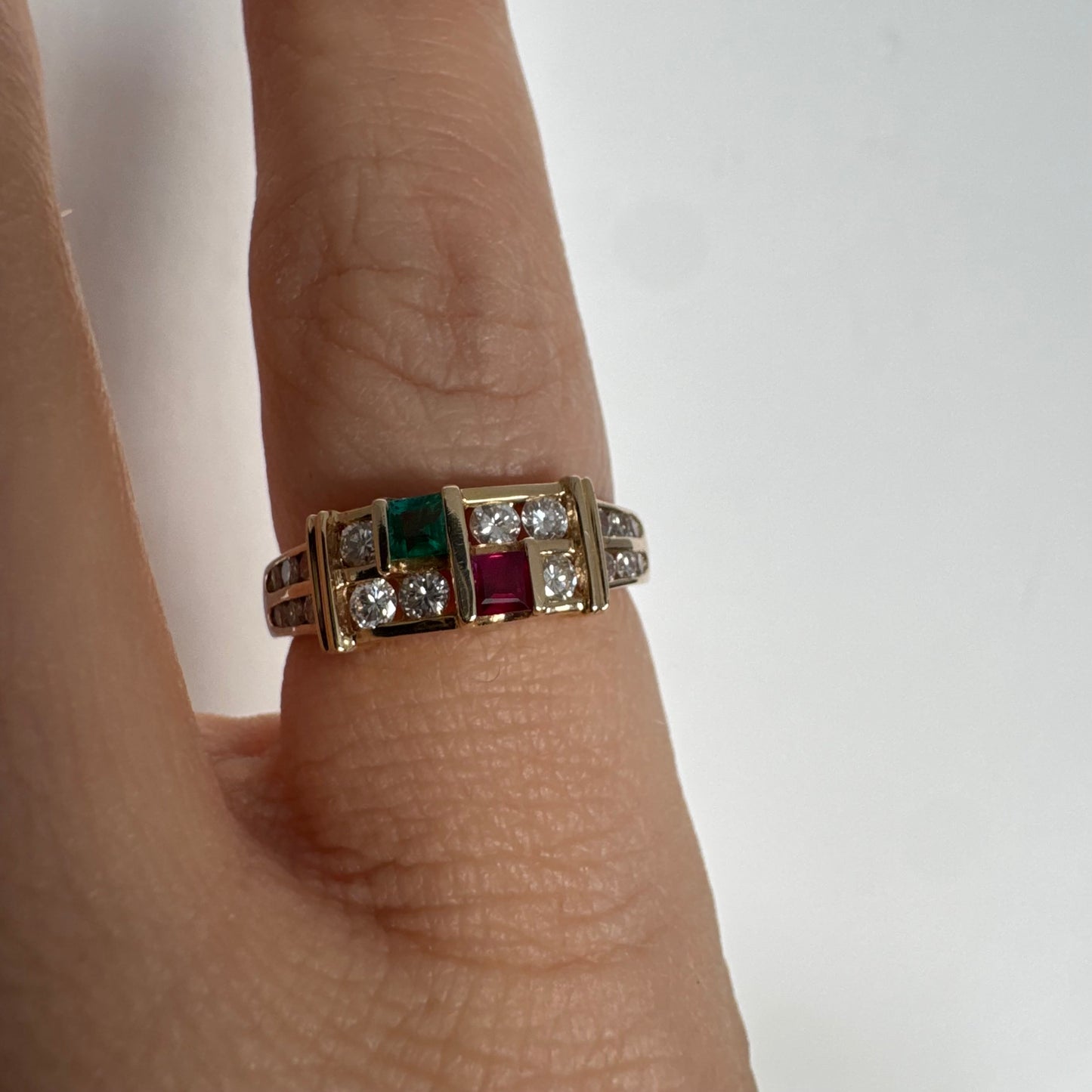 טבעת זהב צהוב 18 קראט בעיצוב גאומטרי מדורג, משובצת יהלומים עגולים לצד אבני אמרלד ורובי בחיתוך מלבני.