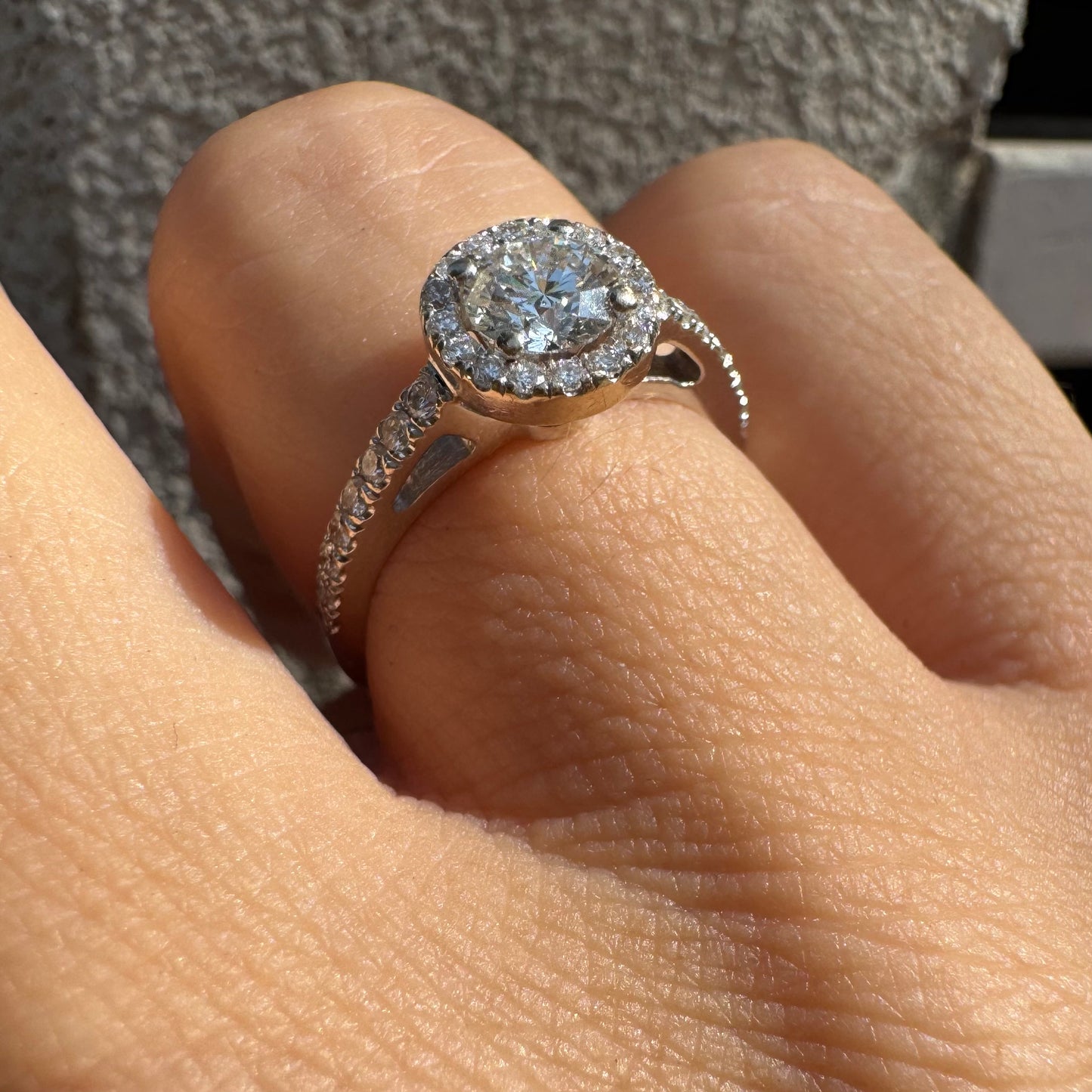 טבעת זהב לבן 14 קראט משובצת יהלום מרכזי עגול והילה נוצצת של יהלומים קטנים, עם יהלומים נוספים על החישוק.