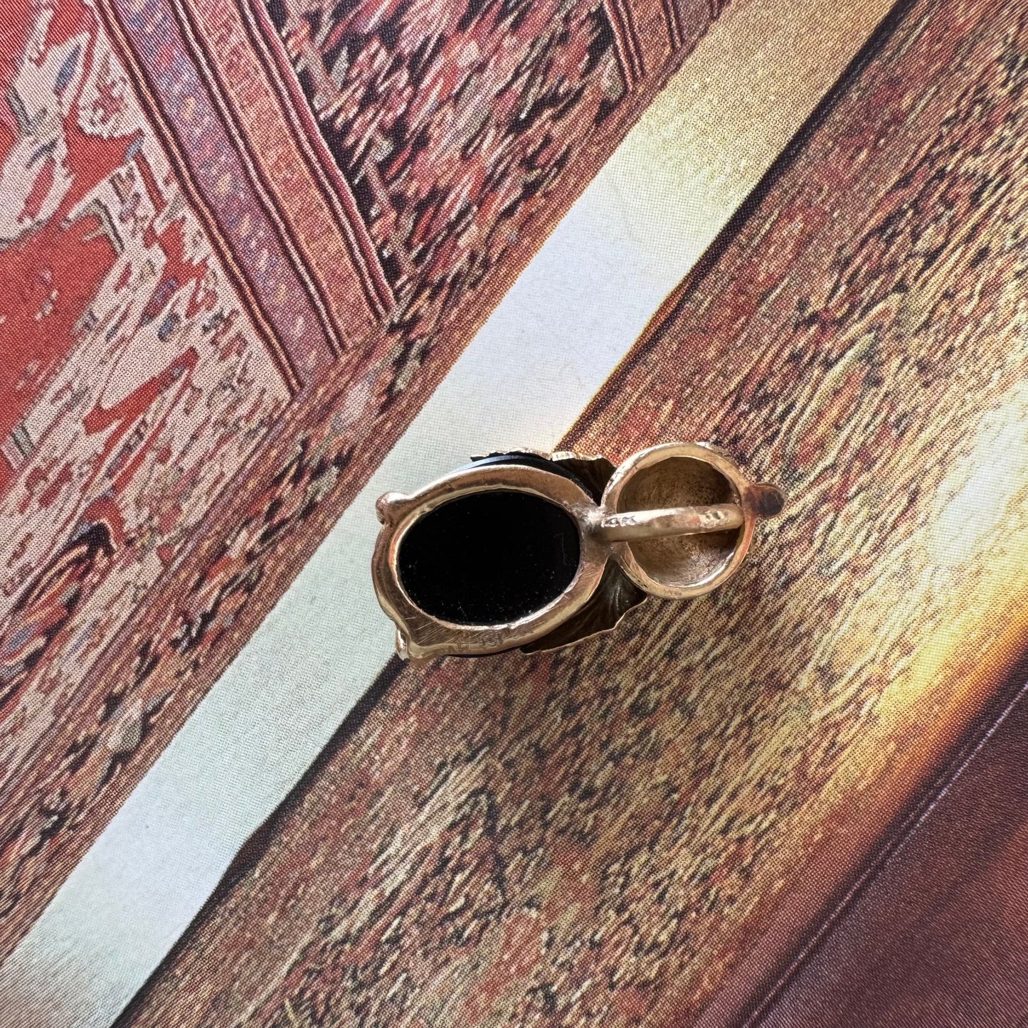 תליון בצורת חיפושית מזהב 14 קראט, עם עיניים אדומות מאבן קורל בחיתוך קבושון וגוף מאבן אוניקס שחורה מבריקה.