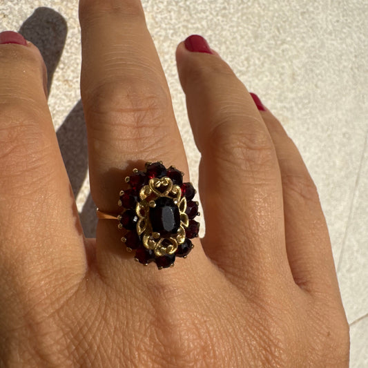 18K gold ring adorned with deep red Garnet gemstones, arranged in a radiant oval composition